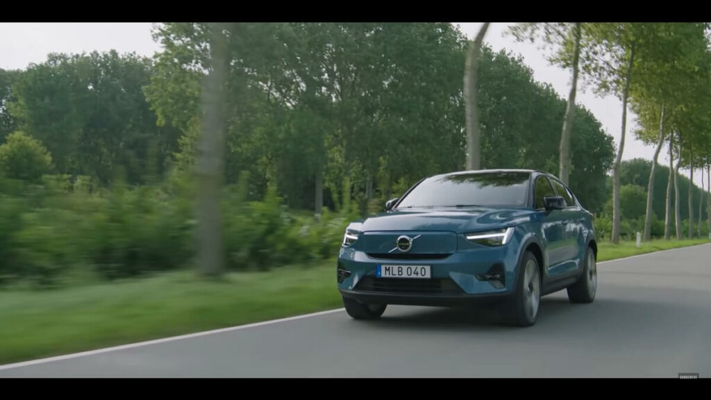 Volvo C40 azul em movimento no asfalto com uma paisagem de floresta.
