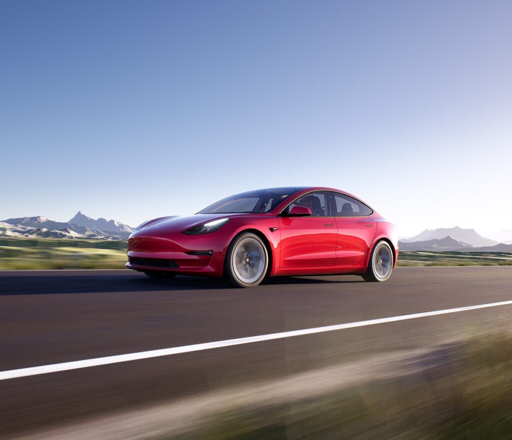 Modelo 3 da Tesla na cor vermelho, com um fundo de estrada