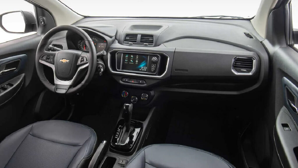 Interior de um Chevrolet Spin 2023 com revestimento em preto, com uma tela multimídia e volante multifuncional. 